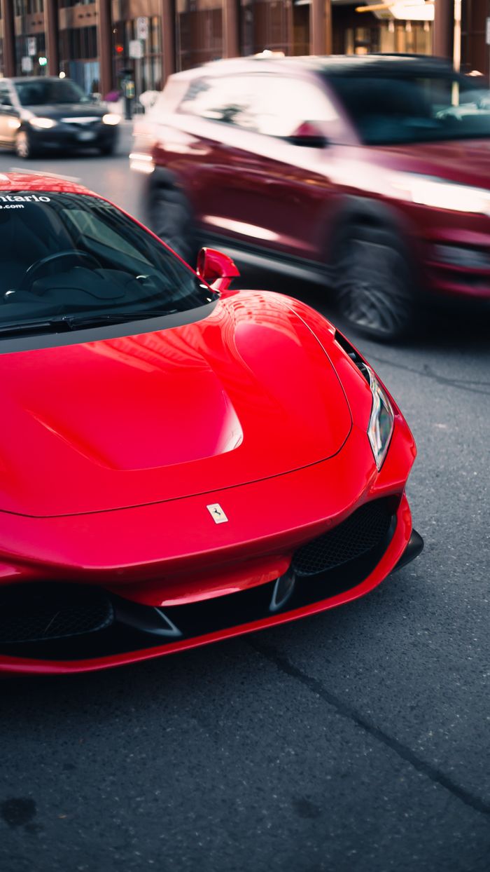 who-we-are A striking red Ferrari supercar parked on a bustling Toronto street, capturing urban elegance.